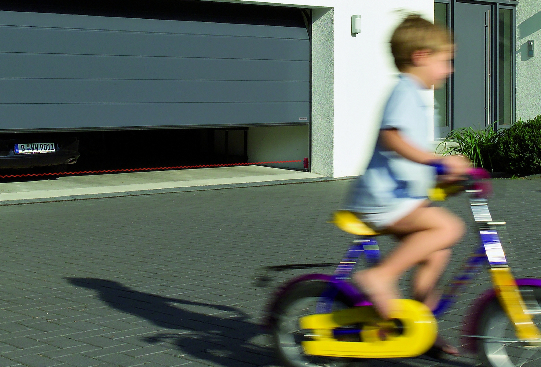 Играющий ребенок перед безопасными гаражными воротами Hörmann с остановочным механизмом.